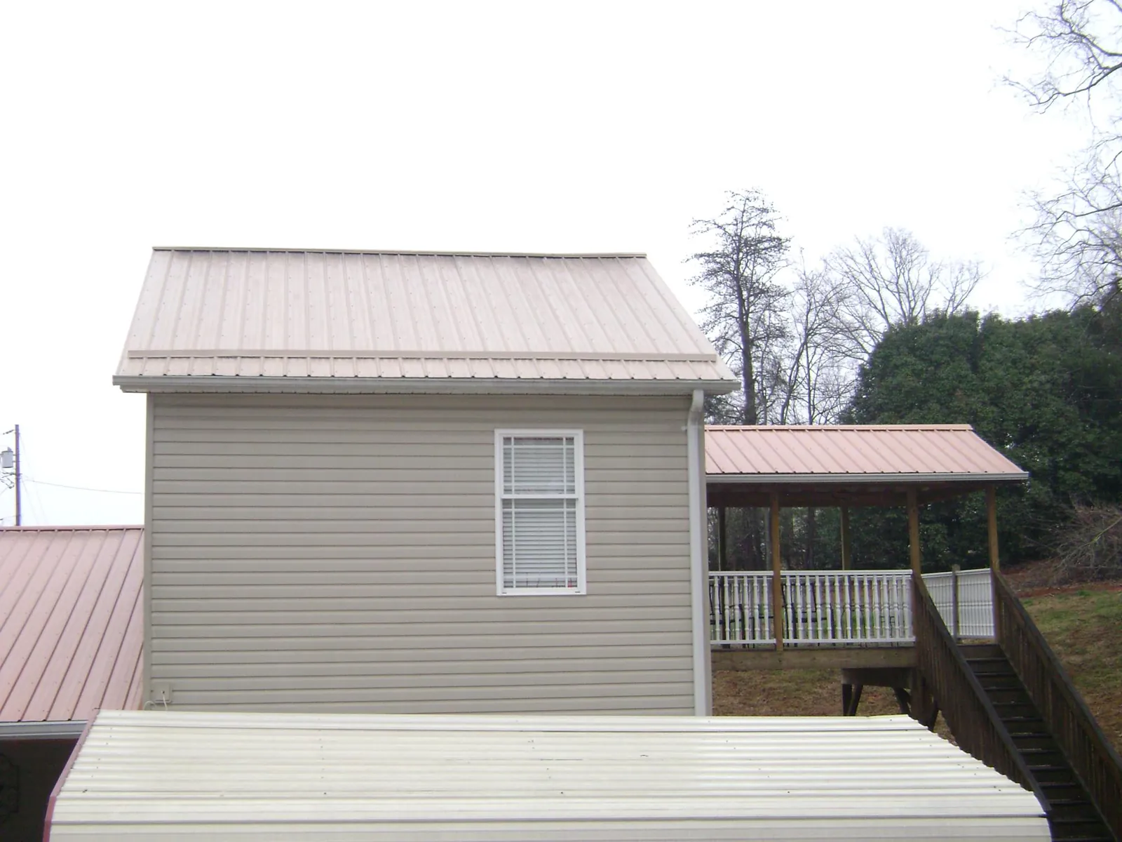 Tan metal roofs on a two story addition and attached porch, from a Roof Replacement job in Newbury